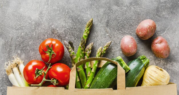 Diferentes vegetales en bolsa de papel sobre gris.