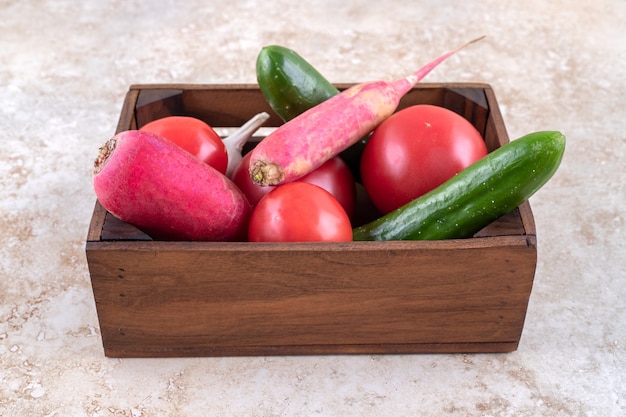 Diferentes verduras en una caja, sobre la mesa de mármol.