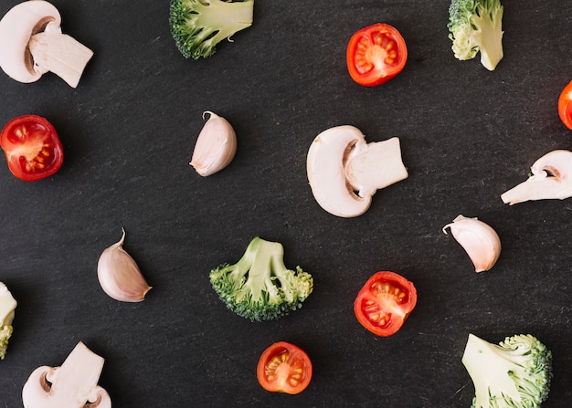 Difundir la seta a la mitad; los tomates brócoli y dientes de ajo sobre fondo negro superficie