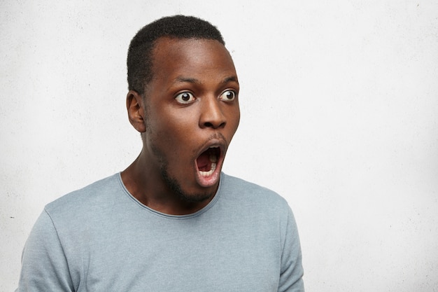 Foto gratuita dios mio. toma de medio perfil de un joven negro divertido con ojos saltones mirando hacia adelante con la boca abierta y la mandíbula caída, toda su mirada expresa sorpresa e incredulidad