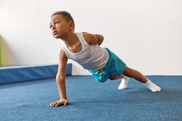 Disciplinado flaco niño afroamericano en ropa deportiva haciendo plancha de brazo único