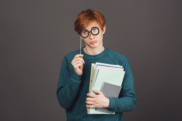 Disculpe señorita, seré un buen chico la próxima vez. Apuesto joven estudiante masculino divertido en cómoda sudadera verde con papeles, mirando a un lado con mirada culpable a través de vasos de papel.