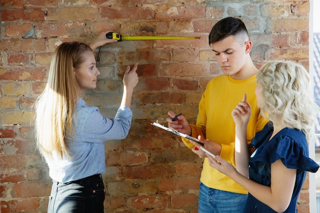 Diseñador de interiores que trabaja con pareja joven. Encantadora familia y diseñador o arquitecto profesional discutiendo el concepto del futuro interior, trabajando con paleta de colores, dibujos de habitaciones en la oficina moderna.