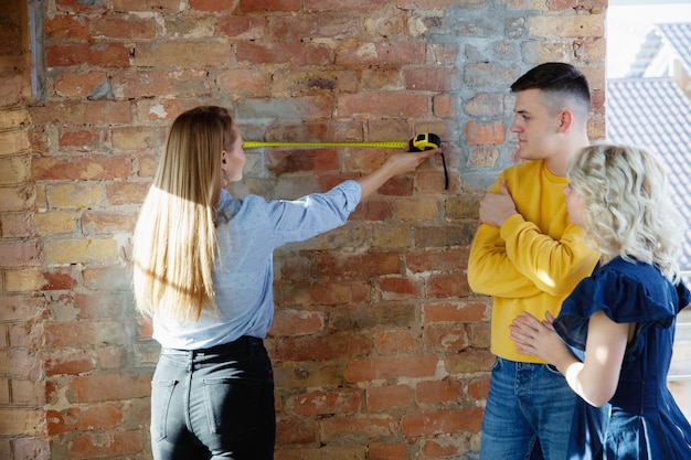 Diseñador de interiores trabajando con pareja joven. Familia encantadora y diseñador o arquitecto profesional discutiendo el concepto del futuro interior, trabajando con paleta de colores, dibujos de habitaciones en la oficina moderna.