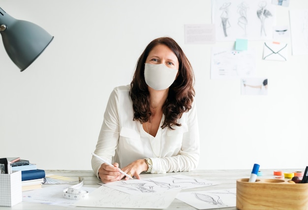 Diseñador en una máscara en el nuevo lugar de trabajo de oficina normal