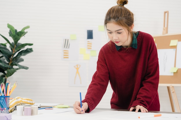 Diseñador de moda femenina asiática hermosa profesional trabajando con bocetos de tela