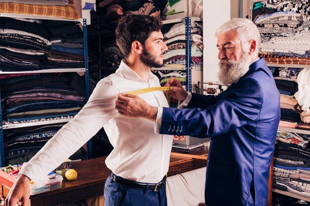 Diseñador de moda masculino profesional que mide el pecho de su cliente.