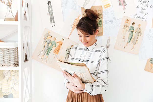 Diseñador de moda mujer sosteniendo cuaderno de bocetos mientras está de pie en su estudio