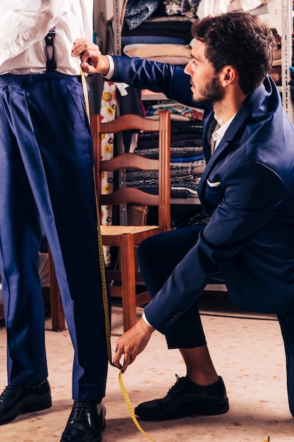 Diseñador de moda que toma la medida del pantalón del cliente masculino en la tienda