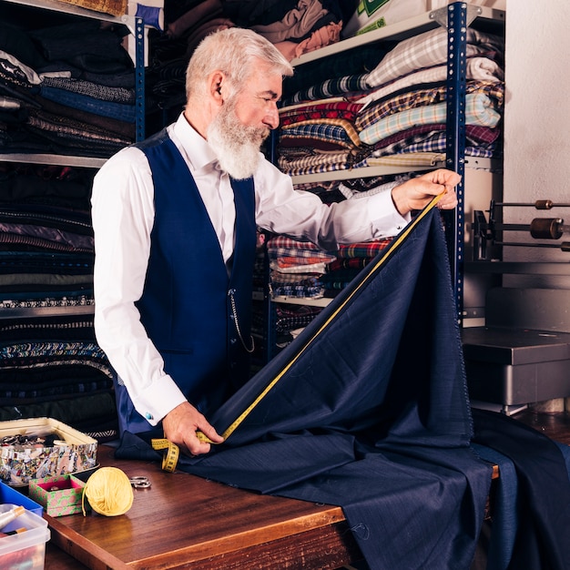 Diseñador de moda que toma la medida de la tela azul con la cinta métrica en la tabla