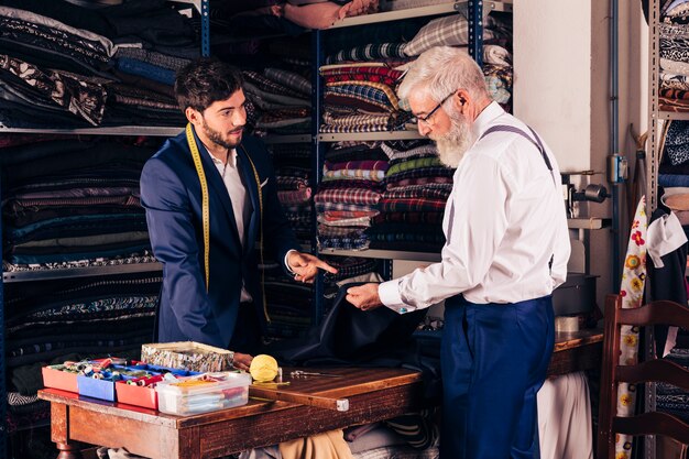 Diseñador de moda de sexo masculino joven que muestra la tela azul a su cliente en la tienda