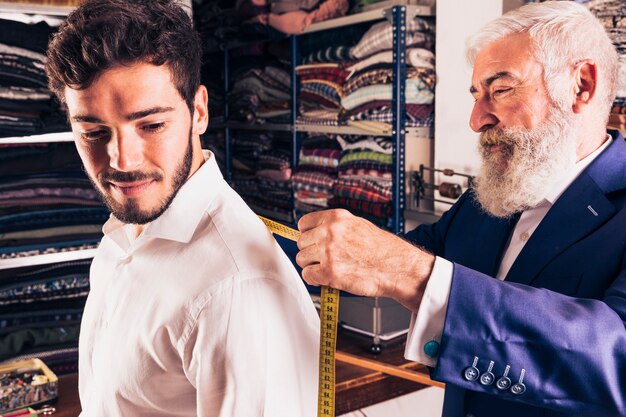 Diseñador de moda de sexo masculino mayor que toma la medida de su cliente en la tienda