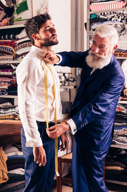 Diseñador de moda de sexo masculino mayor que toma medidas del hombre en su tienda