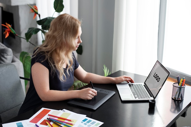 Diseñadora de logotipos trabajando en su tableta conectada a una computadora portátil