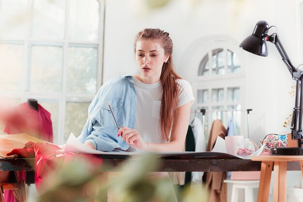 La diseñadora de moda femenina que trabaja en el estudio sentado en el escritorio