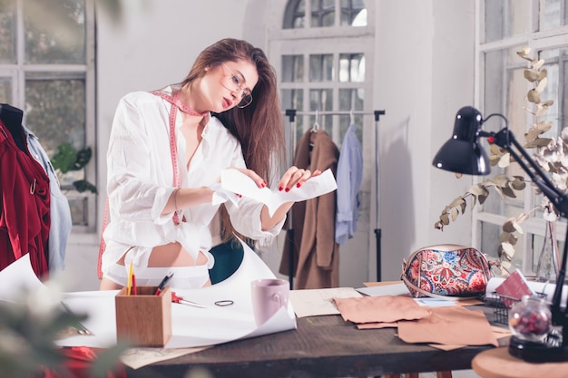 La diseñadora de moda femenina que trabaja en el estudio sentado en el escritorio