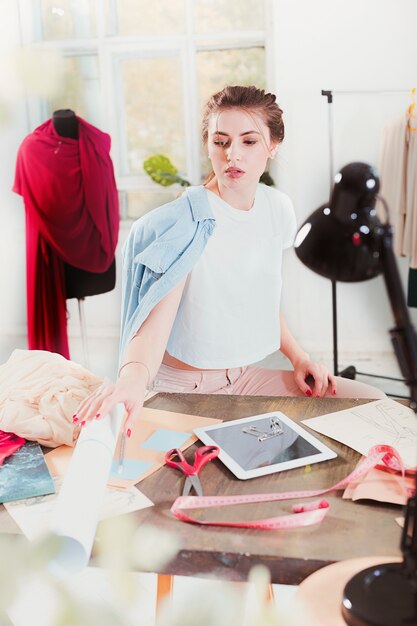 La diseñadora de moda femenina que trabaja en el estudio sentado en el escritorio