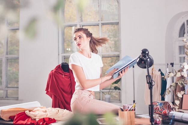 La diseñadora de moda femenina que trabaja en el estudio sentado en el escritorio