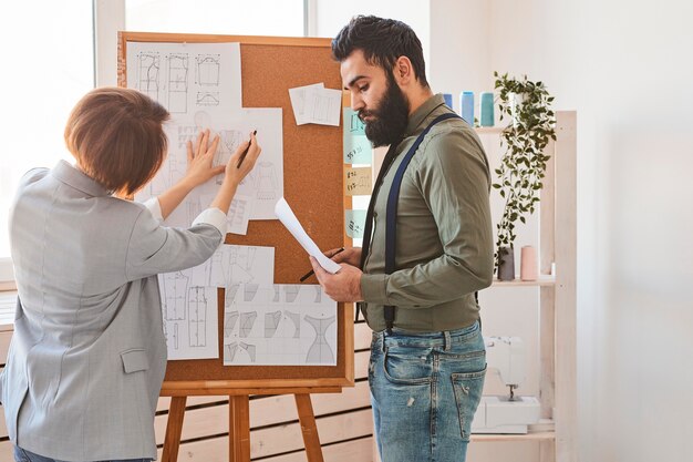 Diseñadores de moda en atelier consultando planes de líneas de ropa en el tablero de ideas