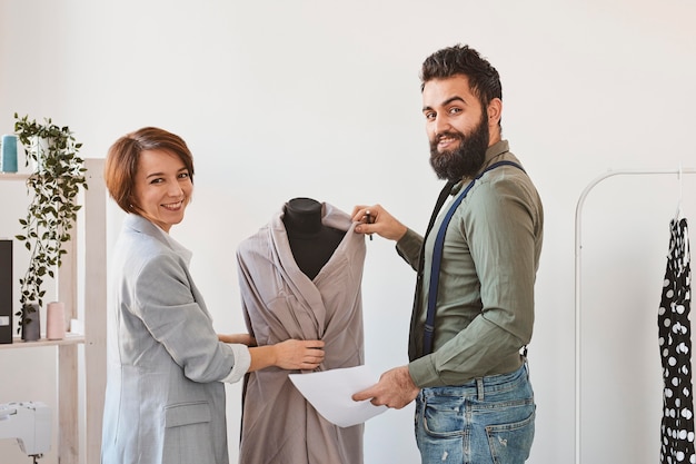 Diseñadores de moda sonrientes en atelier con forma de vestido