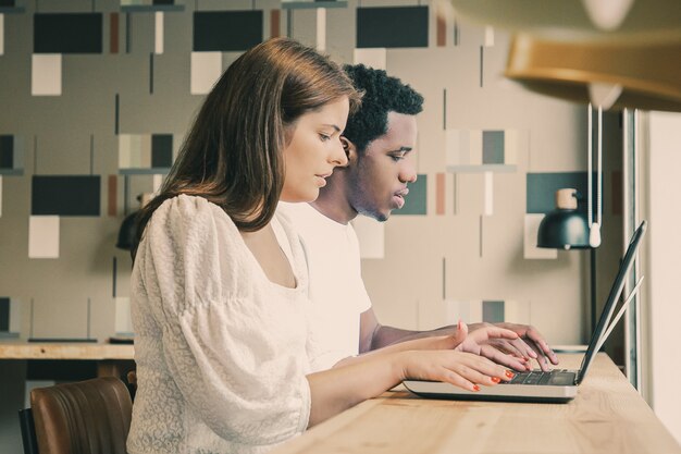 Diseñadores multiétnicos sentados juntos y trabajando en portátiles en el espacio de coworking