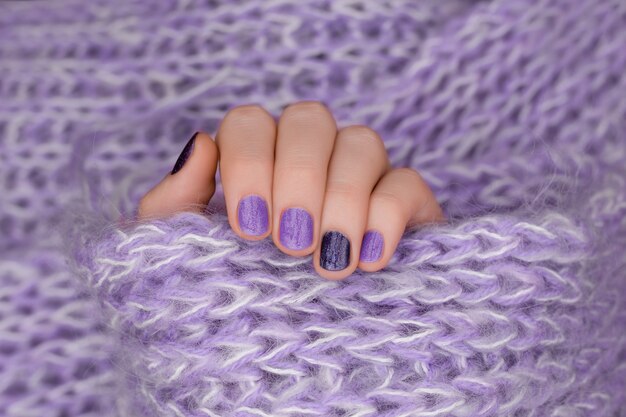 Diseño de uñas morado. Cuidados mano femenina sobre fondo morado.