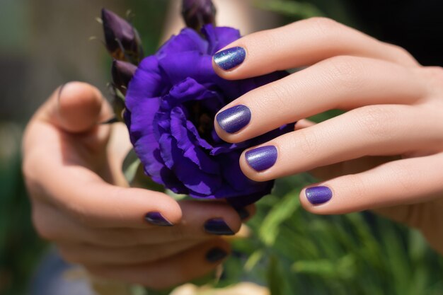 Diseño de uñas morado. Manos femeninas con manicura púrpura con flor de eustoma