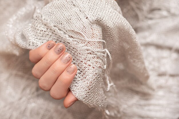 Diseño de uñas con purpurina. Mano femenina con manicura gris.