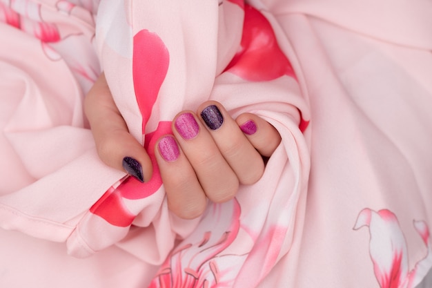 Diseño de uñas rosadas. Cuidados mano femenina sobre fondo rosa.