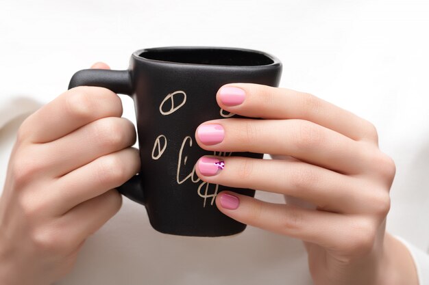 Diseño de uñas rosadas. Manos femeninas que sostienen la taza negra.