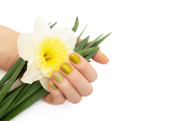 Diseño de uñas verde. Mano femenina con manicura de brillo con flores de narciso.