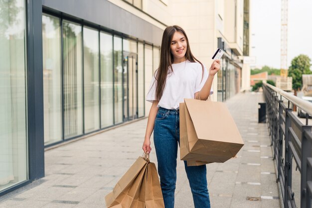 Disfrutando de las compras del día. Longitud total de mujer joven sosteniendo bolsas de la compra y sonriendo mientras camina por la calle