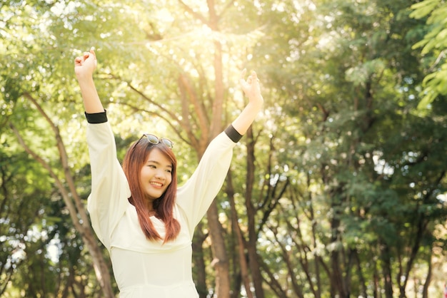 Disfrutando de la naturaleza Brazos asiáticos jovenes de la mujer aumentados disfrutando del aire fresco en bosque verde.