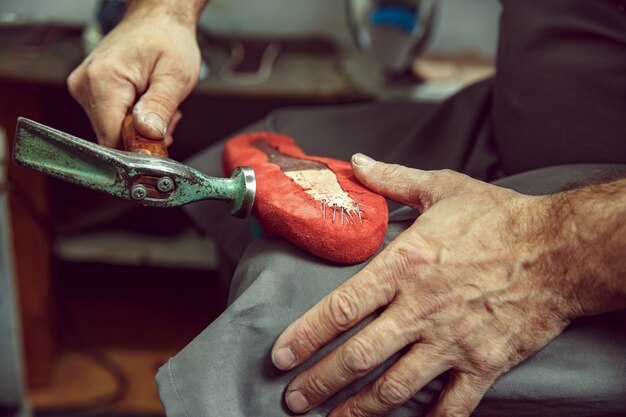 Disfrutando del proceso de creación de zapatos artesanales. Lugar de trabajo de diseñador de calzado. Manos de zapatero tratando con herramienta de zapatero, cerrar