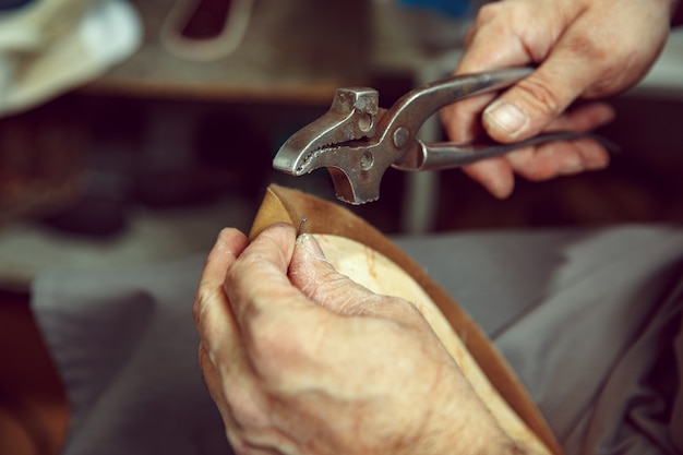 Disfrutando del proceso de creación de zapatos artesanales. Lugar de trabajo de diseñador de calzado. Manos de zapatero tratando con herramienta de zapatero, cerrar