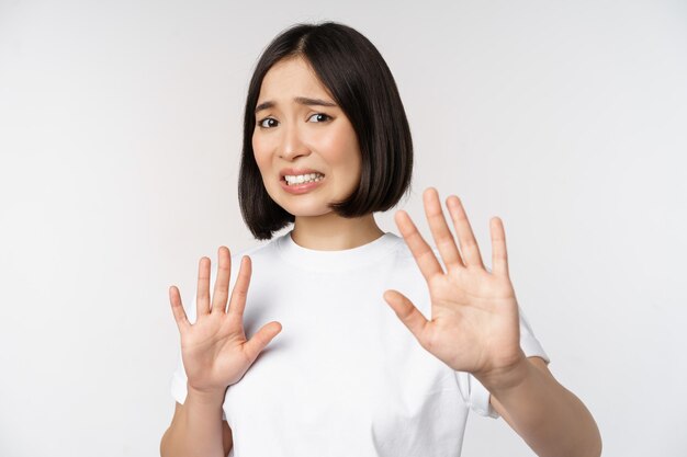 Disgustada mujer asiática rechazando algo haciendo muecas de disgusto y aversión mirando con estremecimiento rechazando la oferta de pie sobre fondo blanco.