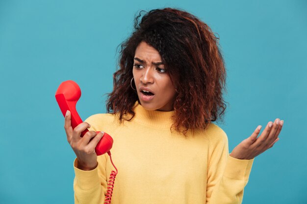 Disgustado confundido joven africana hablando por teléfono.