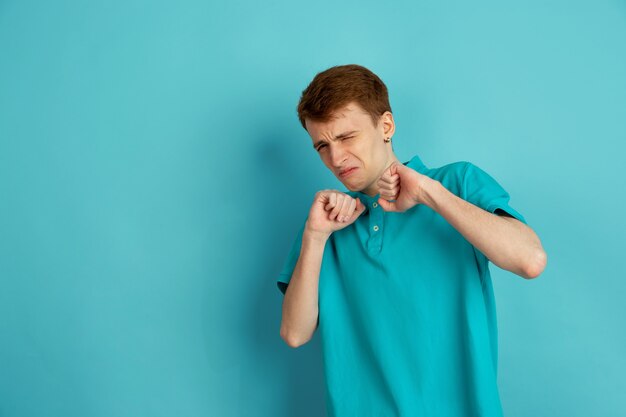 Disgustado, enojado. Retrato moderno del hombre joven caucásico aislado en la pared azul, monocromo. Hermoso modelo masculino. Concepto de emociones humanas, expresión facial, ventas, publicidad, moda.