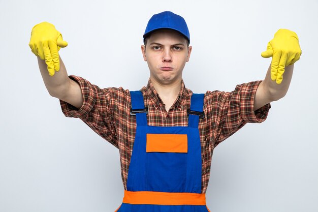 Disgustado fingiendo sostener algo joven chico de limpieza con uniforme y gorra con guantes