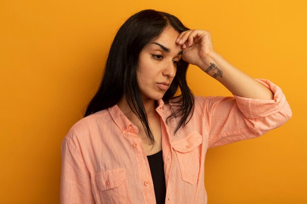 Disgustado mirando al lado hermosa joven vestida con camiseta rosa poniendo la mano en la frente aislada en la pared amarilla