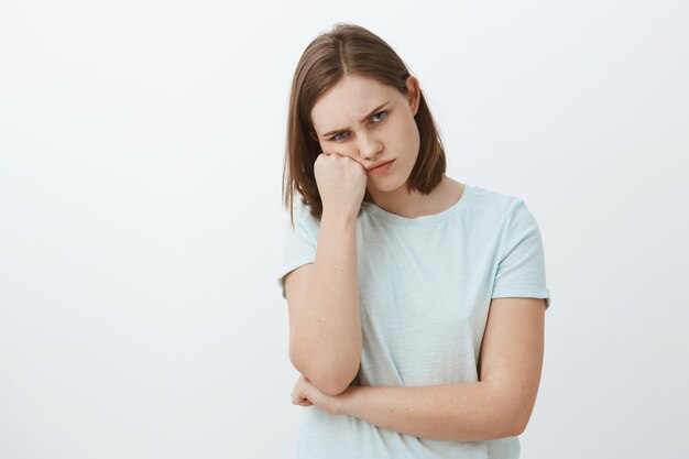 disgustado ofendido y triste linda mujer morena en camiseta con la cara inclinada en el puño frunciendo el ceño y frunciendo los labios sintiendo envidia o celoso viendo hermano recibido increíble regalo de los padres