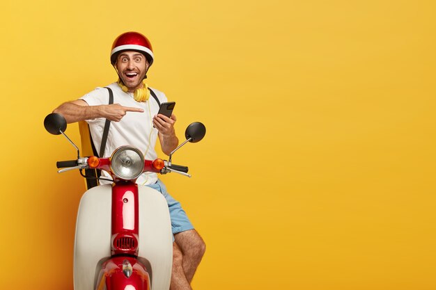 Disparo aislado de feliz guapo conductor masculino en scooter con casco rojo