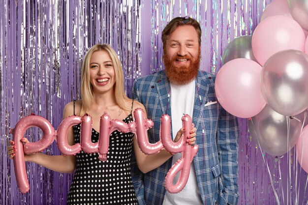 Disparo aislado de feliz mujer rubia con vestido de lunares, alegre hombre pelirrojo en traje formal, sostenga globos de aire, párese de cerca