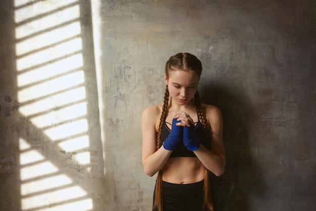 Disparo aislado de hermosa joven profesional de kickboxer europeo serio con dos trenzas con vendas y elegante traje deportivo