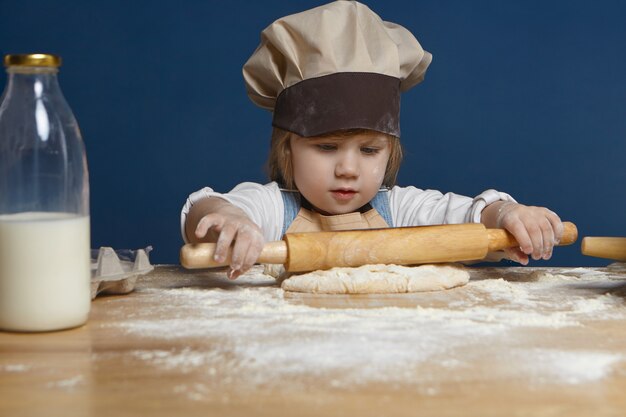 Disparo aislado de hermosa niña de apariencia europea sosteniendo un rodillo mientras hace galletas u otros pasteles en el taller culinario