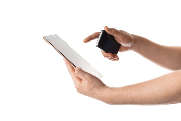 Foto gratuito disparo aislado de manos sosteniendo una tableta y un teléfono en la pared blanca