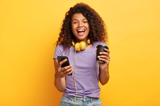 Disparo aislado de mujer joven encantada con peinado afro posando contra la pared amarilla