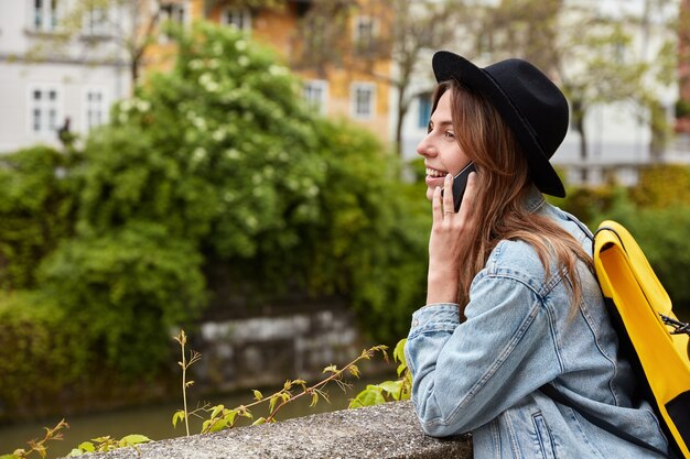 Disparo al aire libre de la bella dama se comunica por celular, admira el maravilloso día y las vistas en la tranquila ciudad