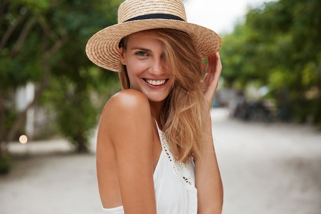 Disparo al aire libre de buena mujer joven feliz con amplia sonrisa brillante, viste ropa elegante de verano