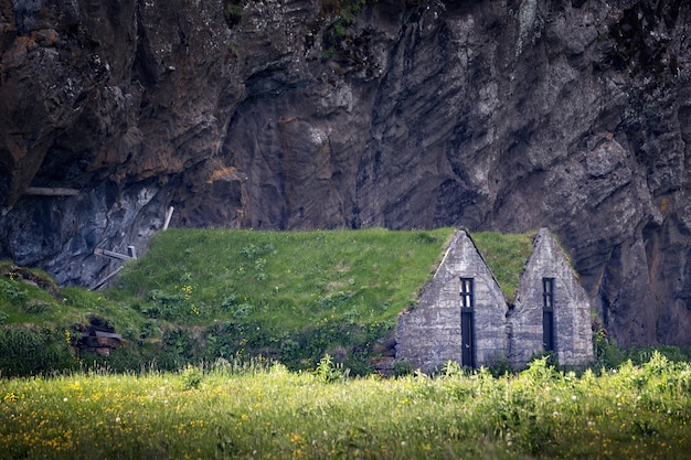 Disparo al nivel de los ojos de dos casas de piedra con techos de pasto en un campo bajo un acantilado en Islandia